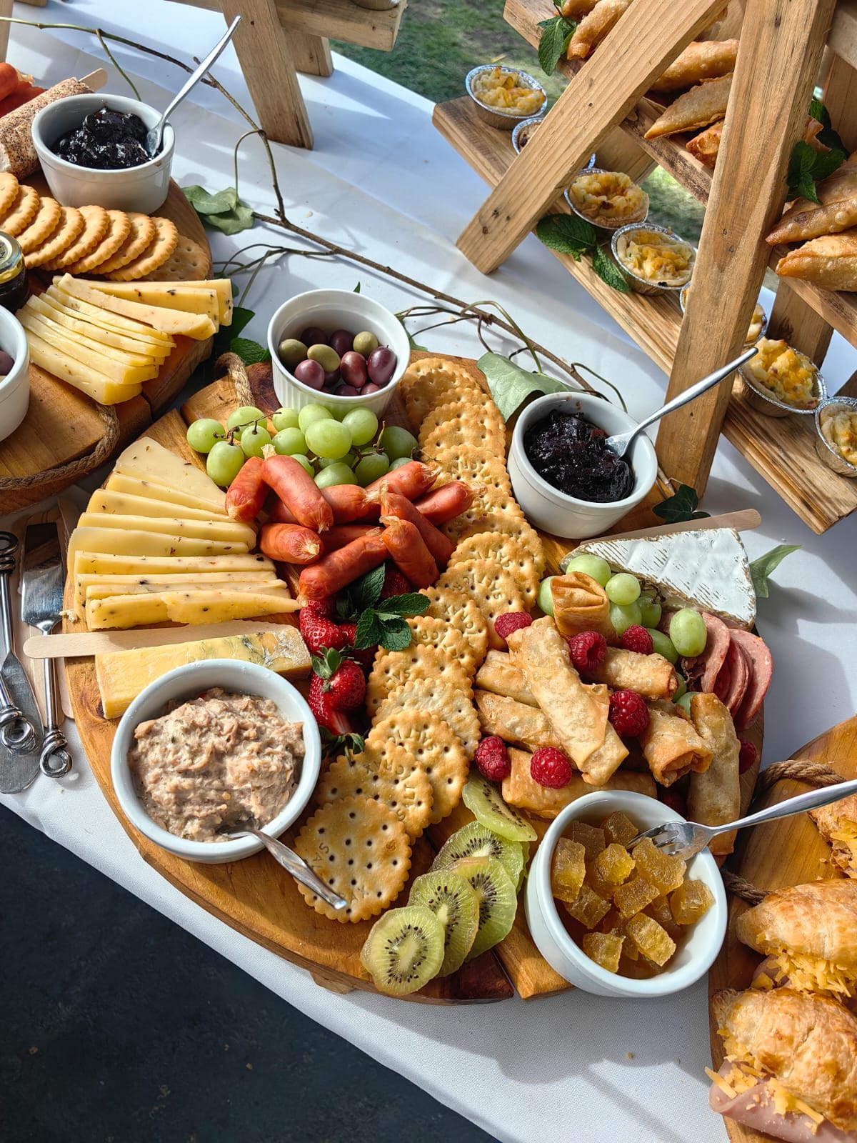 Grazing platter by Creations catering: a wooden board of cheeses, crackers, grapes, strawberries, raspberries, kiwi, olives, spring rolls, mini sausages and dips