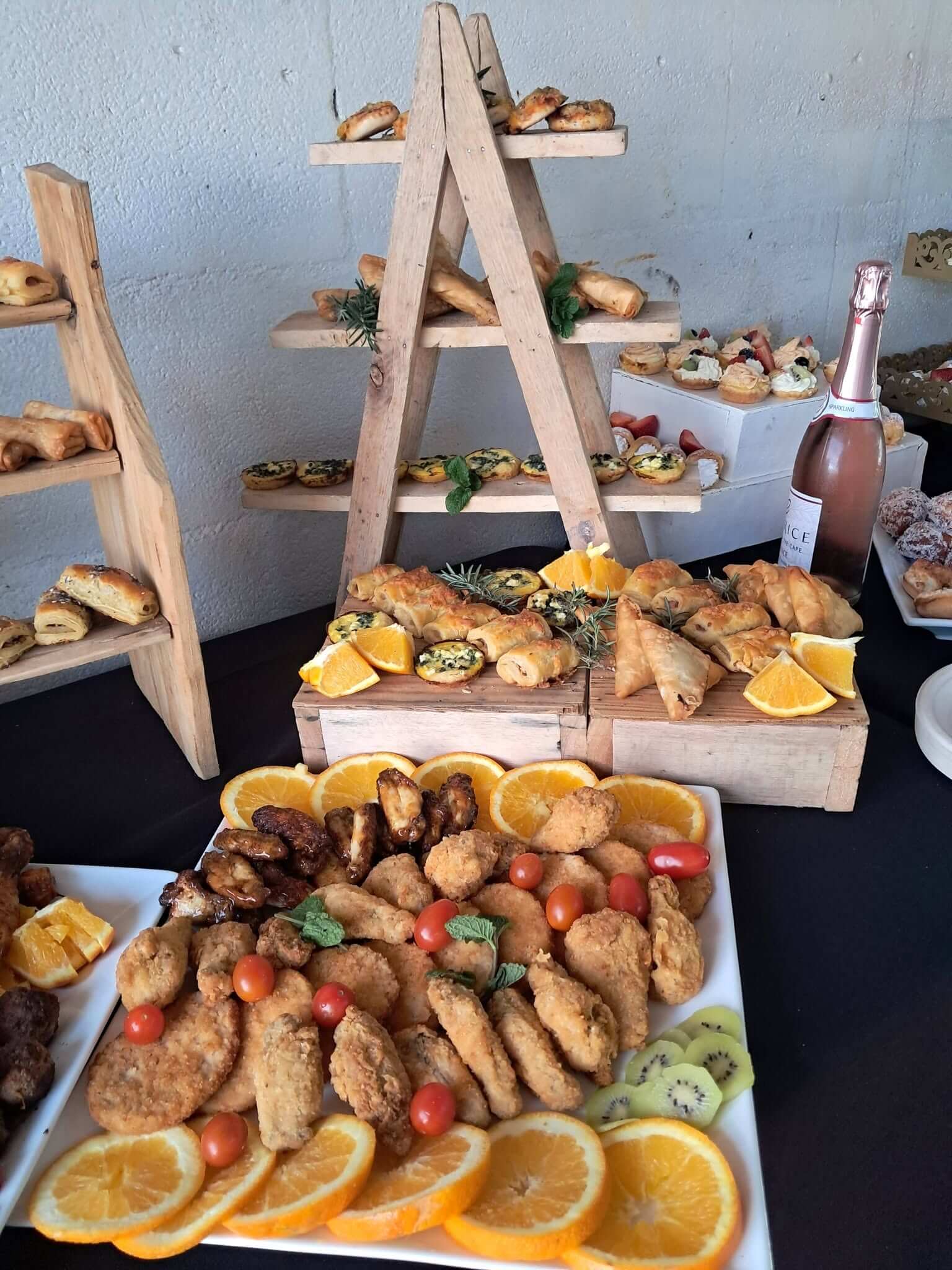 Savoury canape display by Creations catering: wooden ladder stands with mini quiches, samoosas, sausage rolls and pastries, fruit tarts and sparkling wine